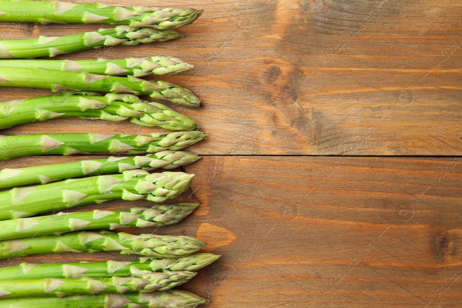 Photo of Fresh green asparagus stems on wooden table, top view. Space for text