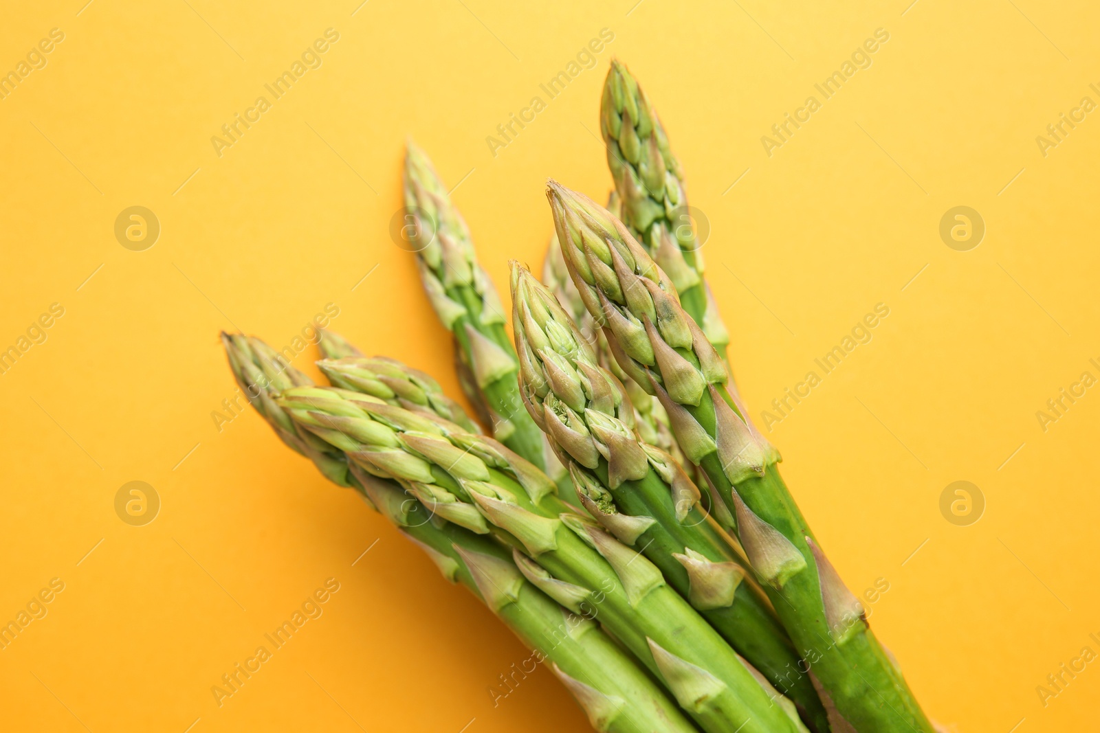 Photo of Fresh green asparagus stems on orange table, top view