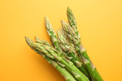 Photo of Fresh green asparagus stems on orange table, top view