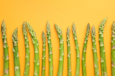 Photo of Fresh green asparagus stems on orange table, top view