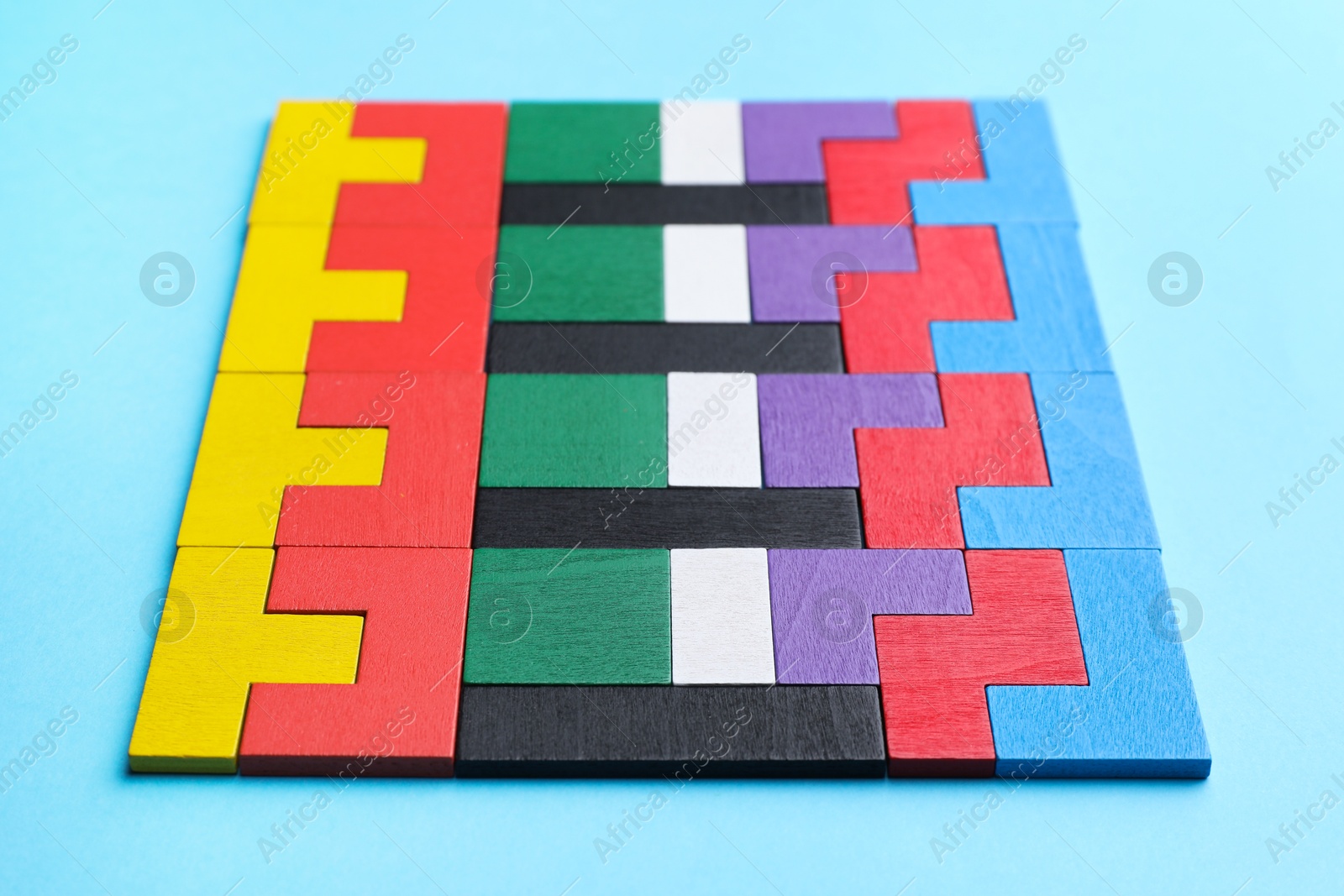 Photo of Colorful wooden puzzle pieces on light blue background, closeup