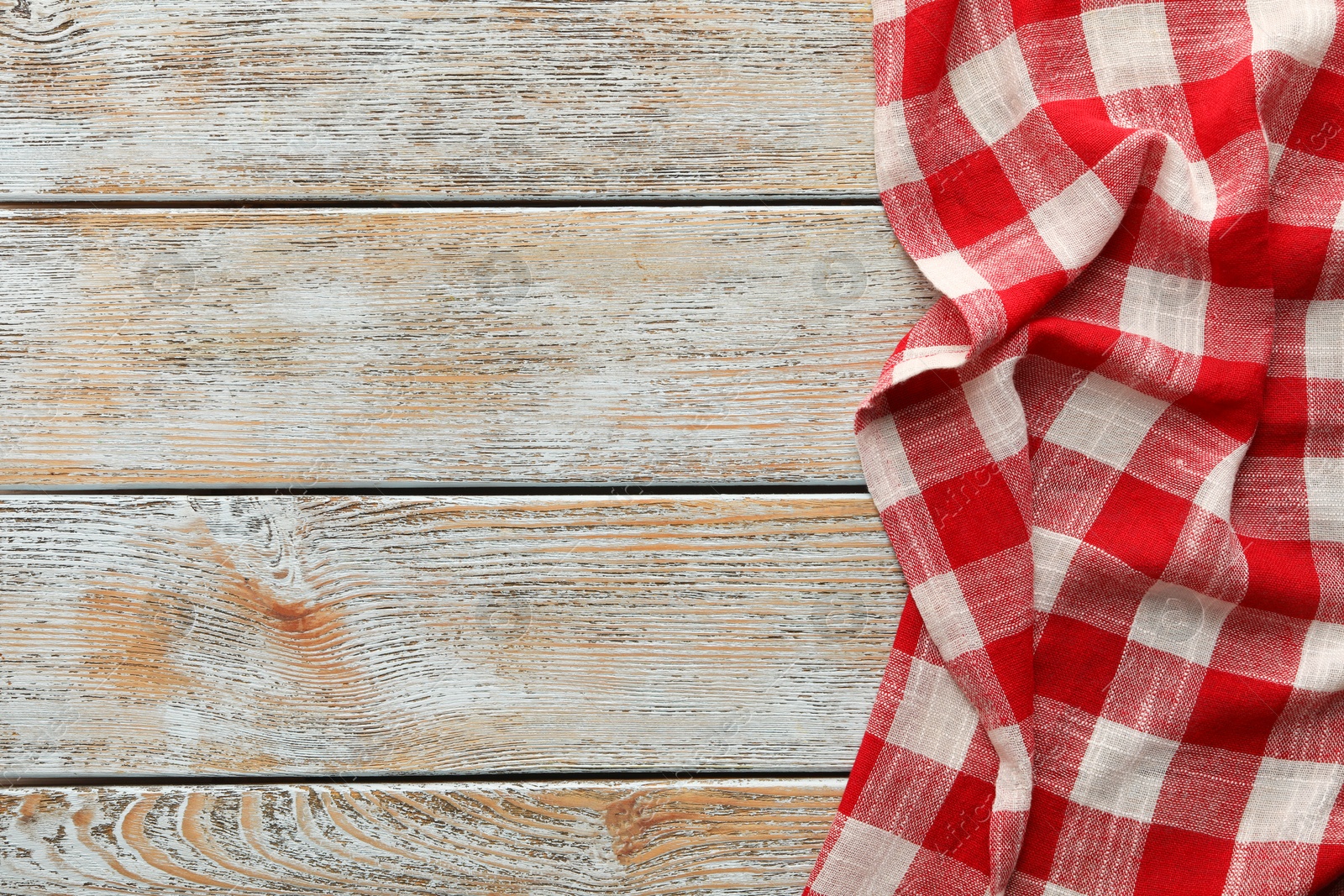 Photo of Red checkered picnic tablecloth on old wooden table, top view. Space for text