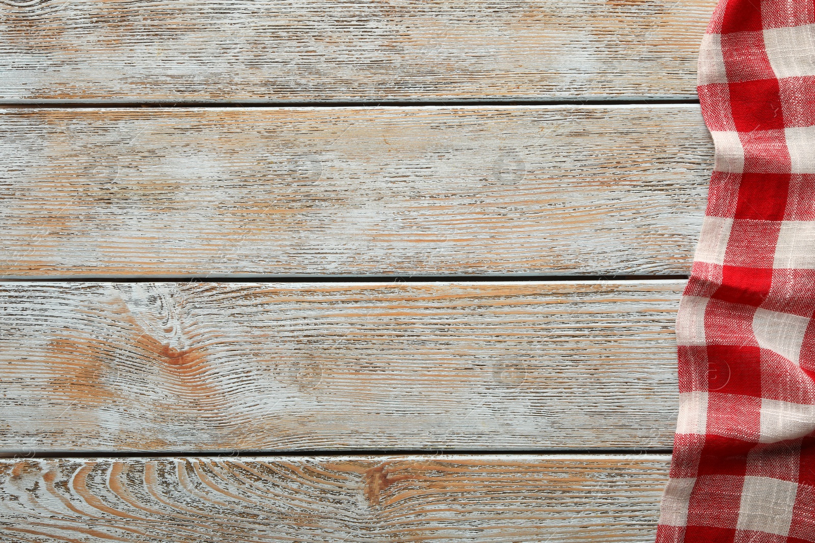 Photo of Red checkered picnic tablecloth on old wooden table, top view. Space for text