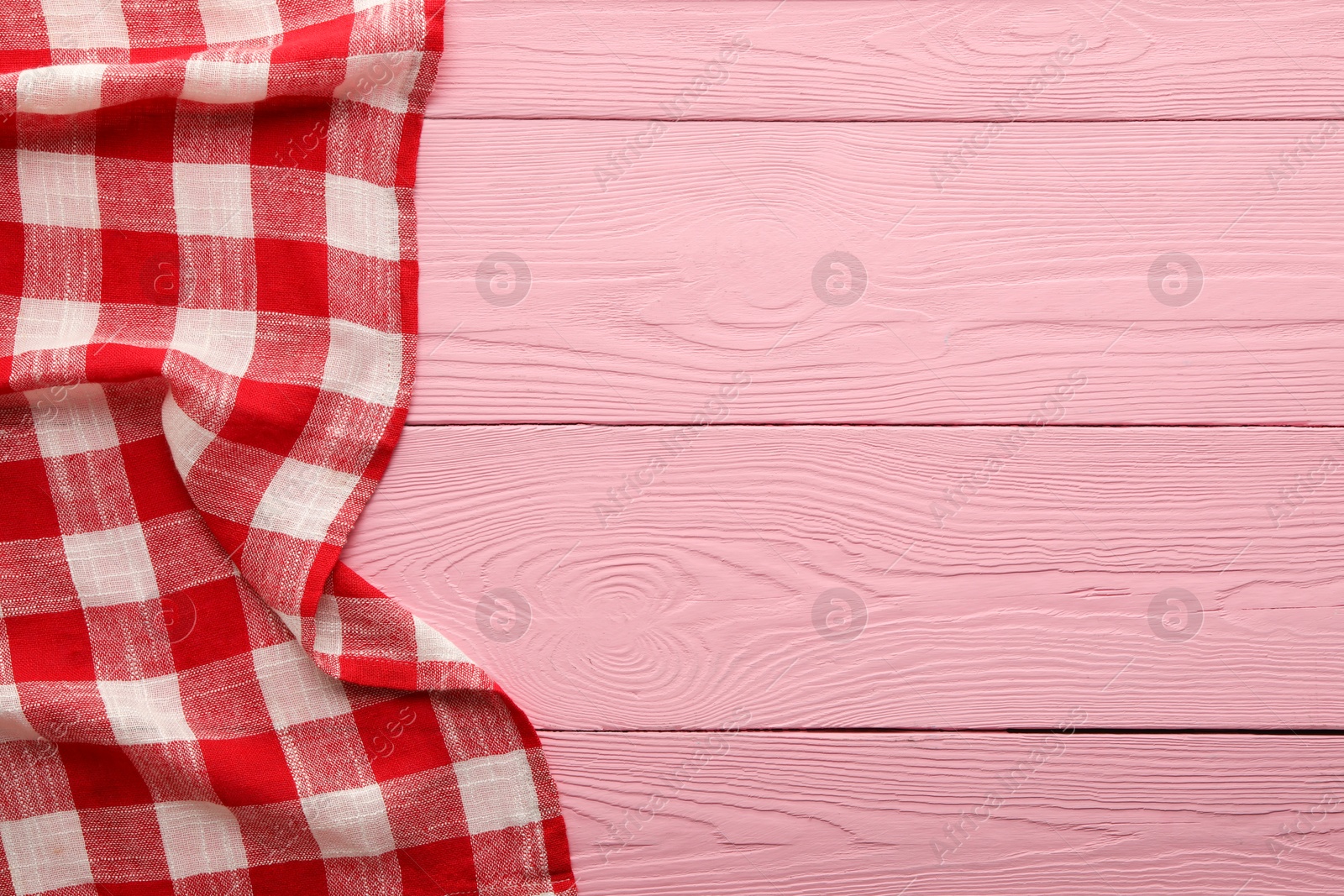 Photo of Red checkered picnic tablecloth on pink wooden table, top view. Space for text