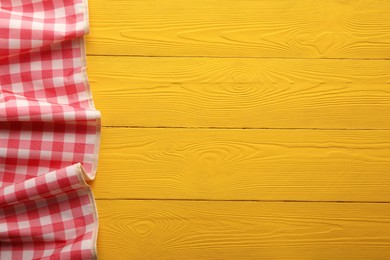 Photo of Red checkered picnic tablecloth on yellow wooden table, top view. Space for text