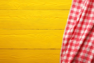 Photo of Red checkered picnic tablecloth on yellow wooden table, top view. Space for text