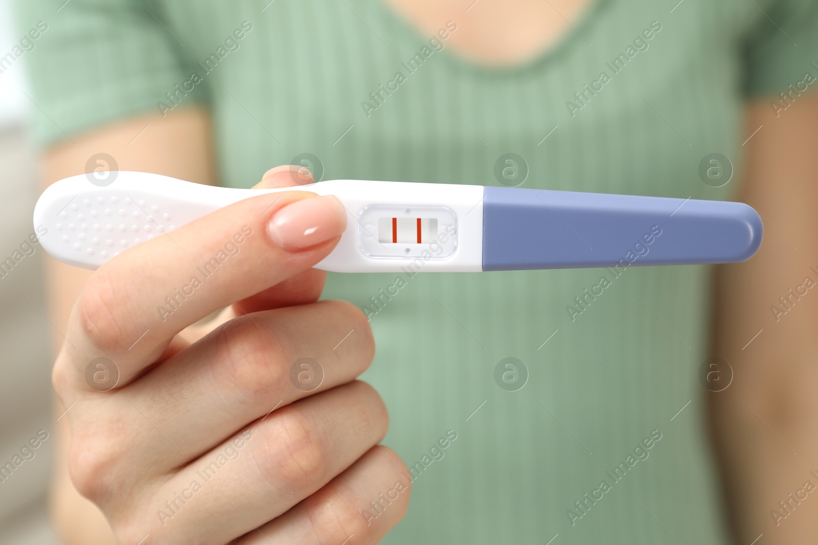 Photo of Woman holding positive pregnancy test indoors, closeup view