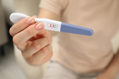 Woman holding positive pregnancy test indoors, closeup view