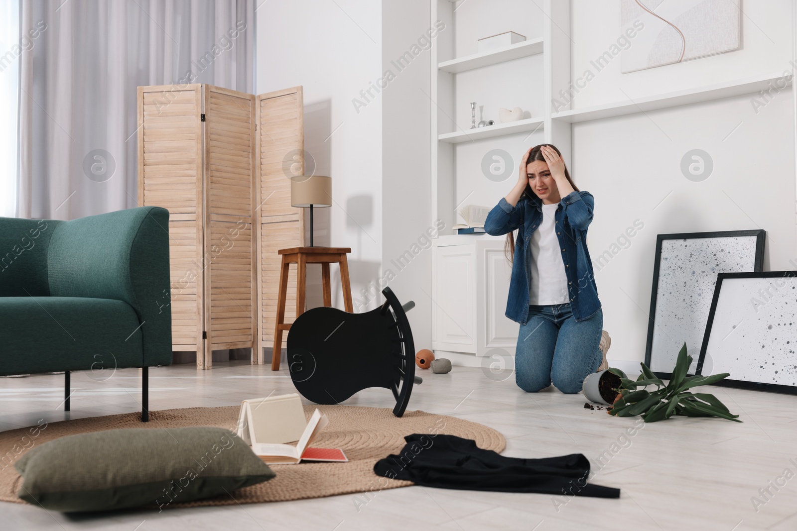 Photo of Desperate woman sitting on floor in messy living room after robbery