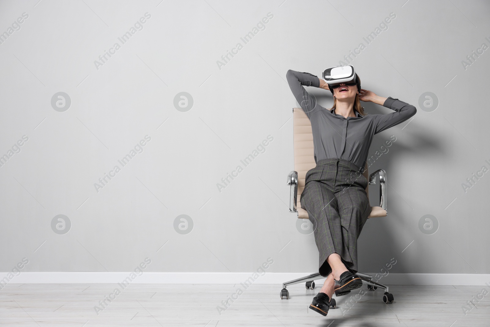 Photo of Happy woman with virtual reality headset sitting on chair indoors, space for text