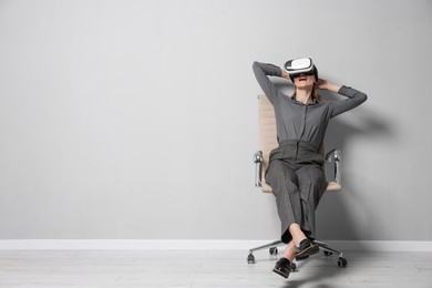 Happy woman with virtual reality headset sitting on chair indoors, space for text