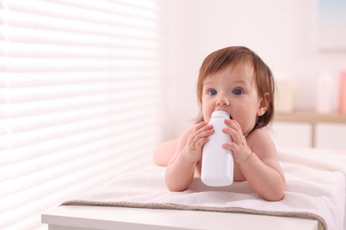 Photo of Cute little girl with bottle of dusting powder on changing table indoors, space for text