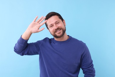 Photo of Cheerful man waving on light blue background