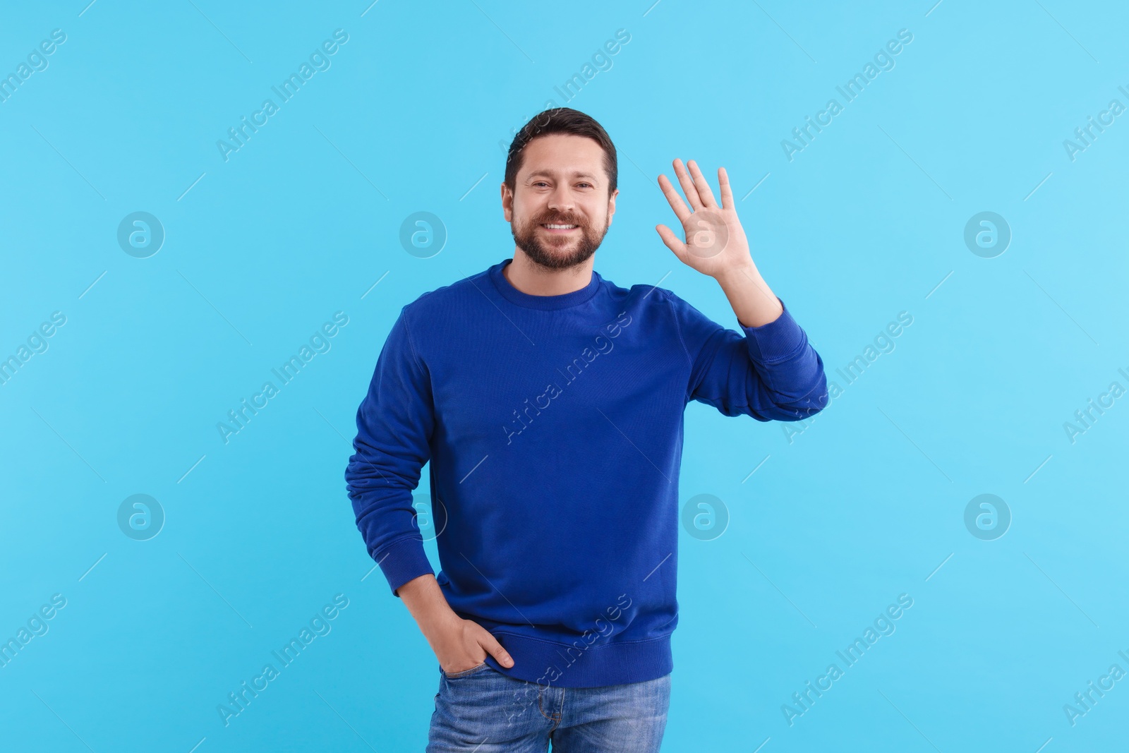 Photo of Cheerful man waving on light blue background