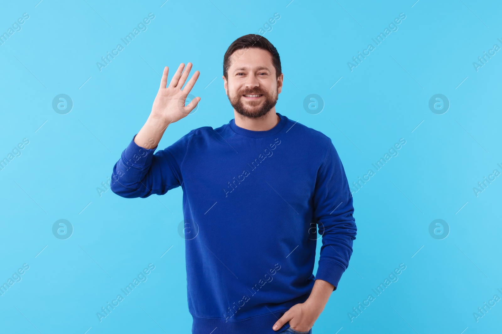 Photo of Cheerful man waving on light blue background