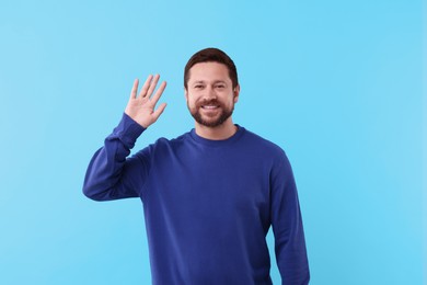 Photo of Cheerful man waving on light blue background