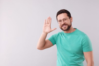 Cheerful man waving on light background. Space for text