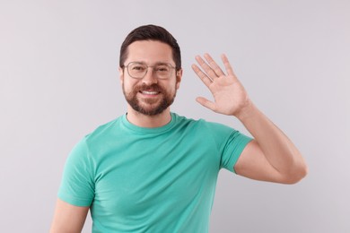 Photo of Cheerful handsome man waving on light background