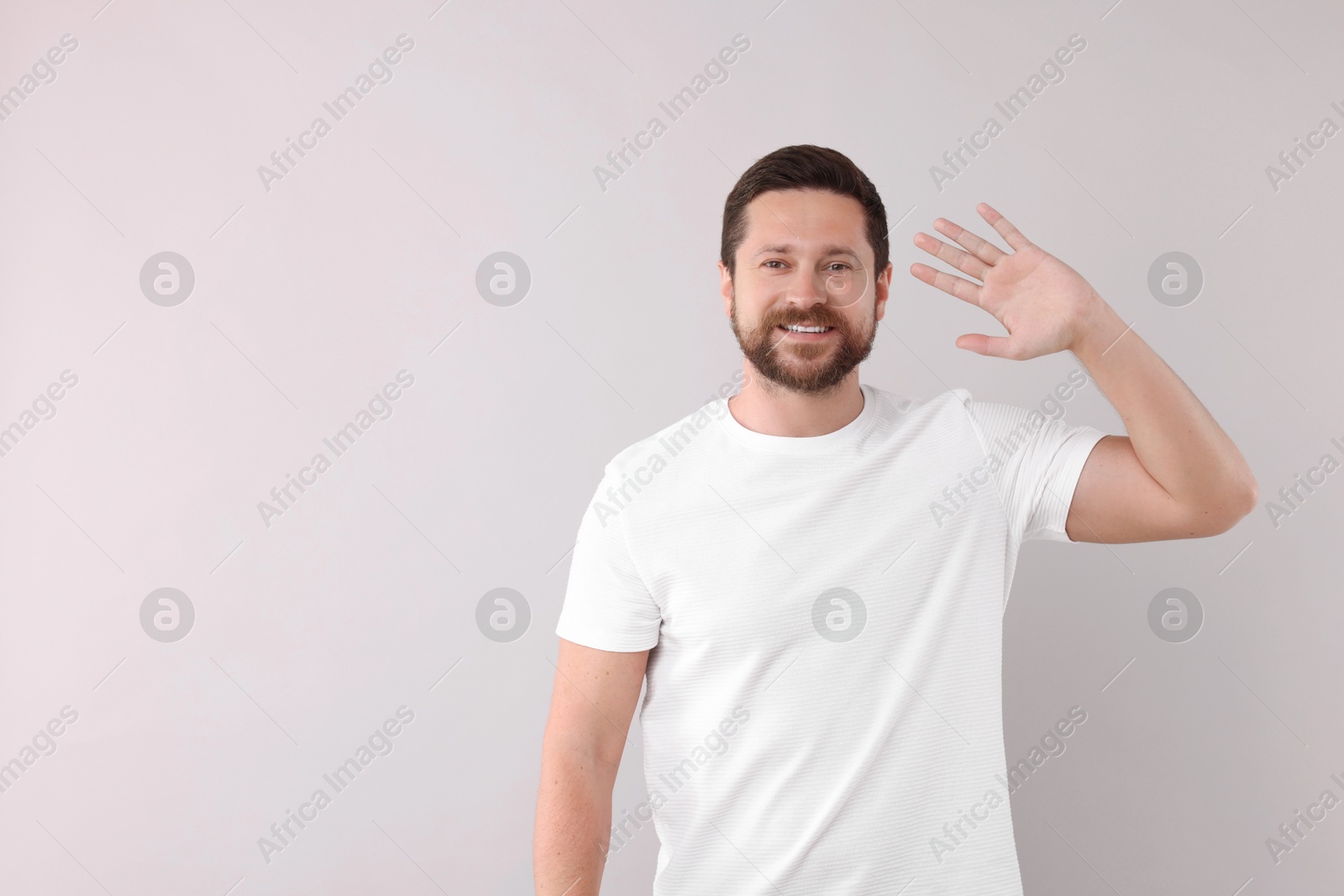 Photo of Cheerful man waving on light background. Space for text