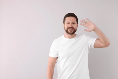 Cheerful man waving on light background. Space for text