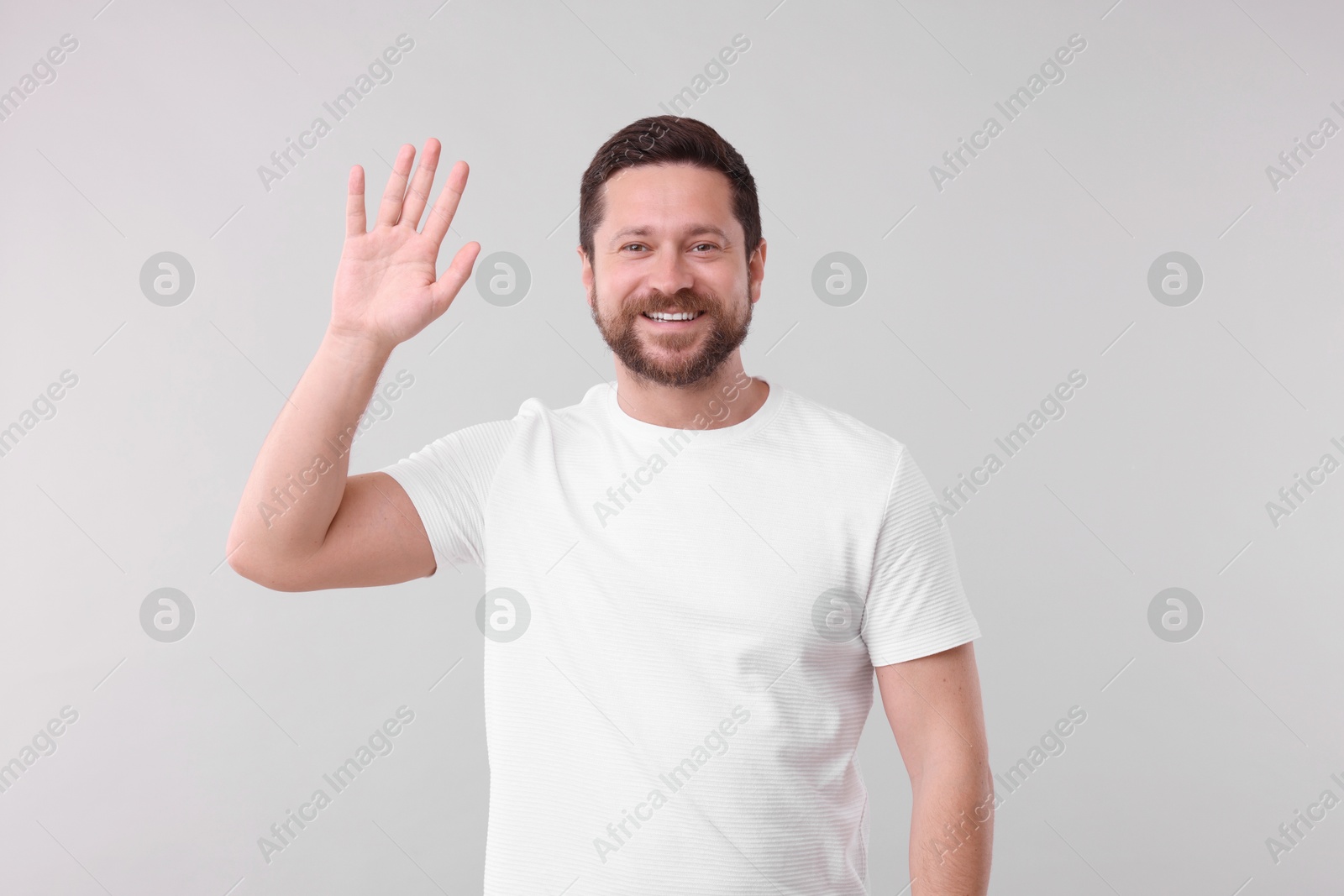 Photo of Cheerful handsome man waving on light background