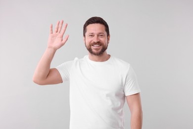 Cheerful handsome man waving on light background