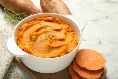 Photo of Delicious mashed sweet potatoes in pot, vegetables and microgreens on white marble table, closeup