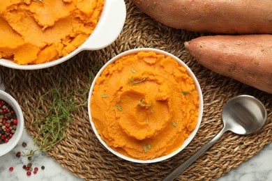 Delicious mashed sweet potatoes in bowl, spoon, microgreens, spices and vegetables on white marble table, top view