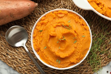 Delicious mashed sweet potatoes in bowl, spoon, microgreens and vegetable on table, top view