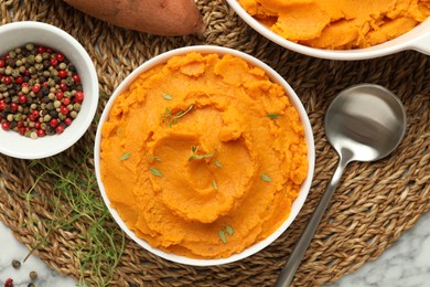 Photo of Delicious mashed sweet potatoes in bowl, spoon, microgreens, spices and vegetable on white marble table, top view