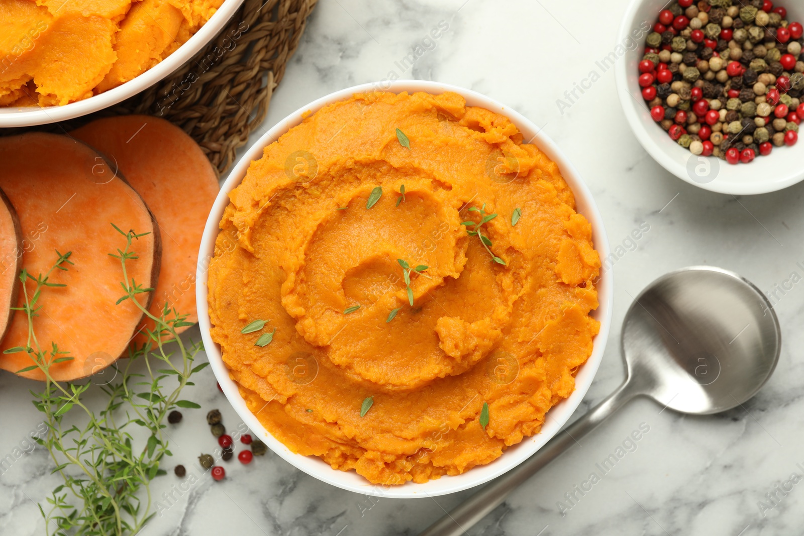 Photo of Delicious mashed sweet potatoes in bowl, spoon, microgreens, spices and vegetable on white marble table, top view