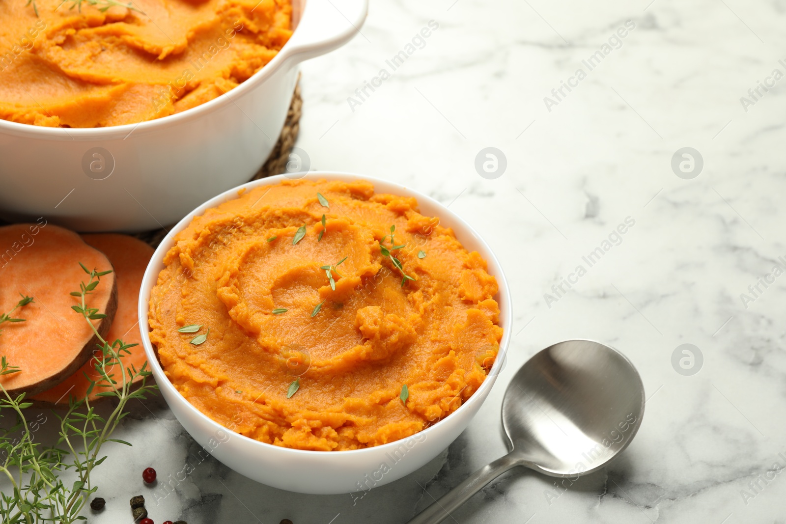 Photo of Delicious mashed sweet potatoes, spoon, microgreens, spices and vegetable on white marble table