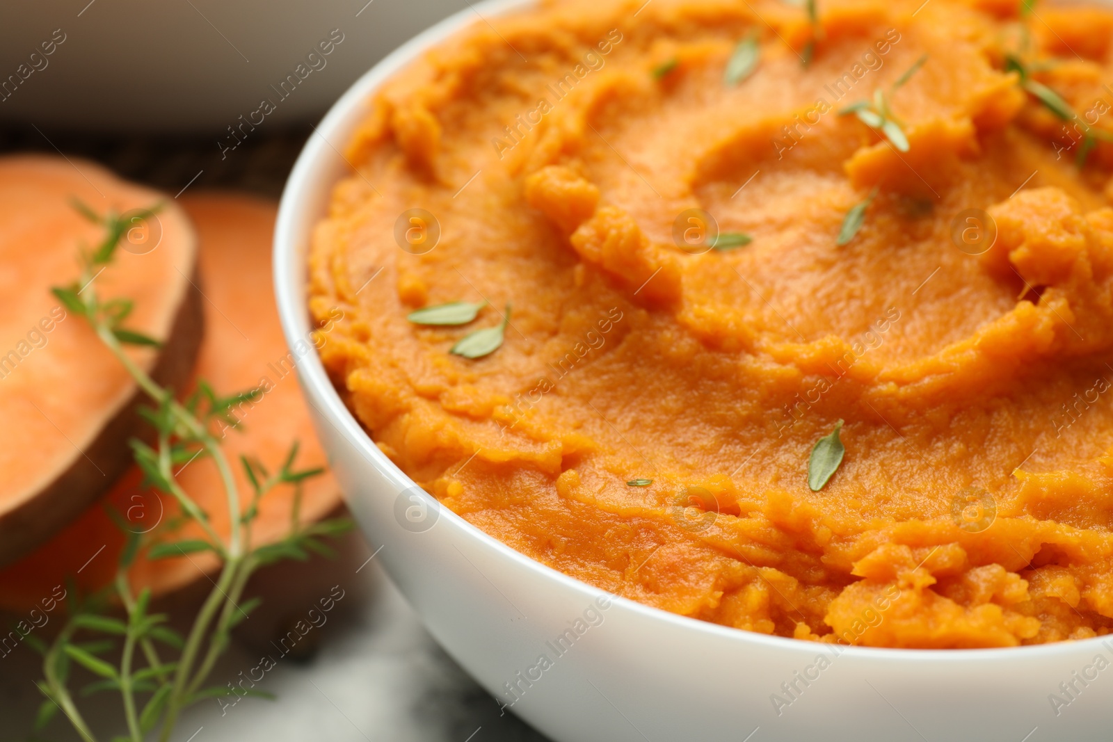 Photo of Delicious mashed sweet potatoes in bowl and microgreens on table, closeup