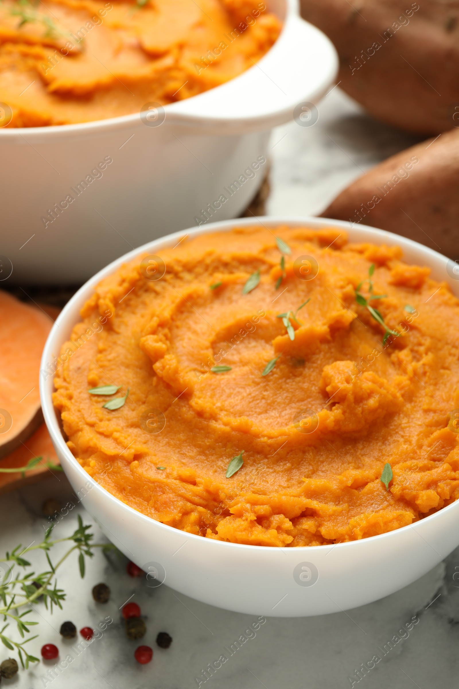 Photo of Delicious mashed sweet potatoes in bowl and spices on white marble table, closeup