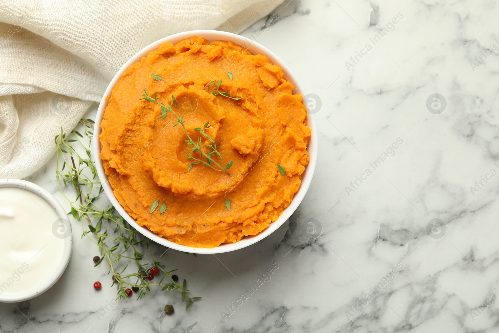 Photo of Delicious mashed sweet potatoes in bowl, microgreens, sour cream and spices on white marble table, top view. Space for text