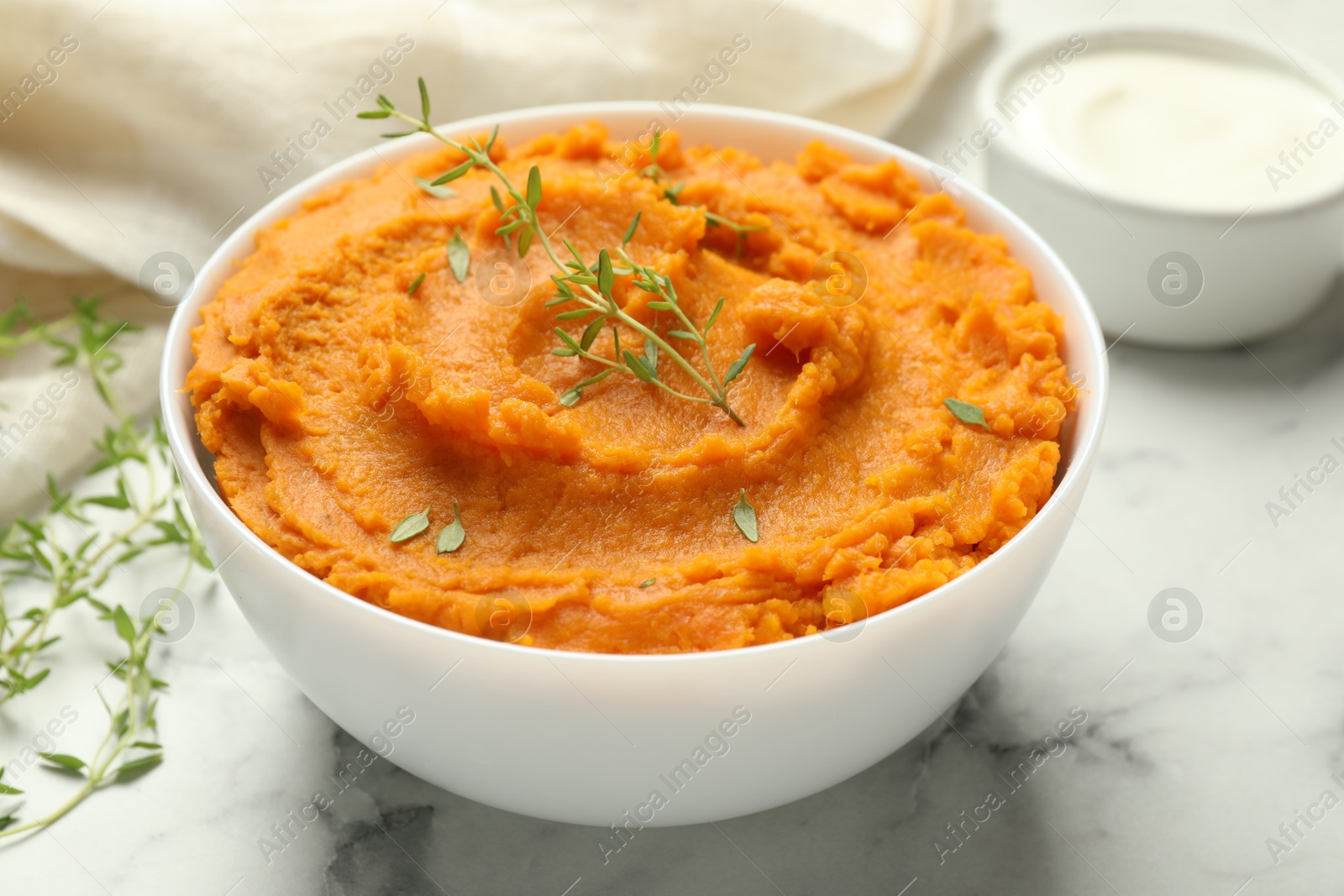 Photo of Delicious mashed sweet potatoes in bowl, microgreens and sour cream on white marble table, closeup