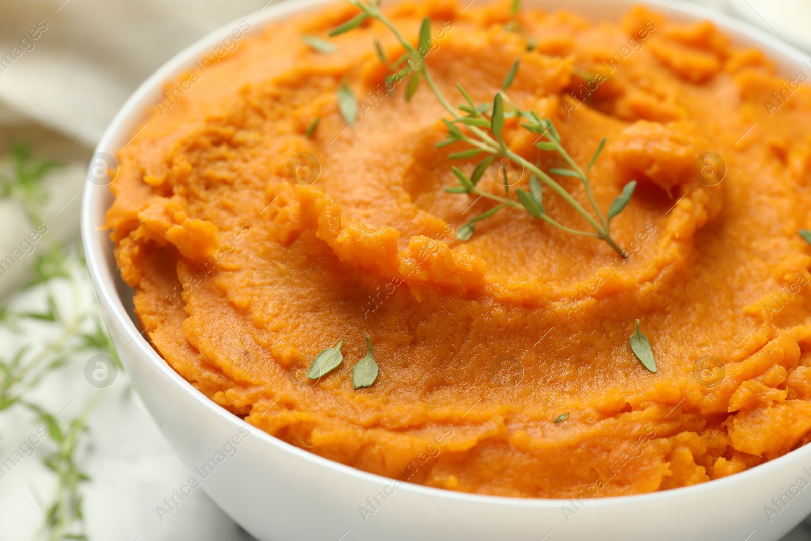 Photo of Delicious mashed sweet potatoes in bowl and microgreens on table, closeup