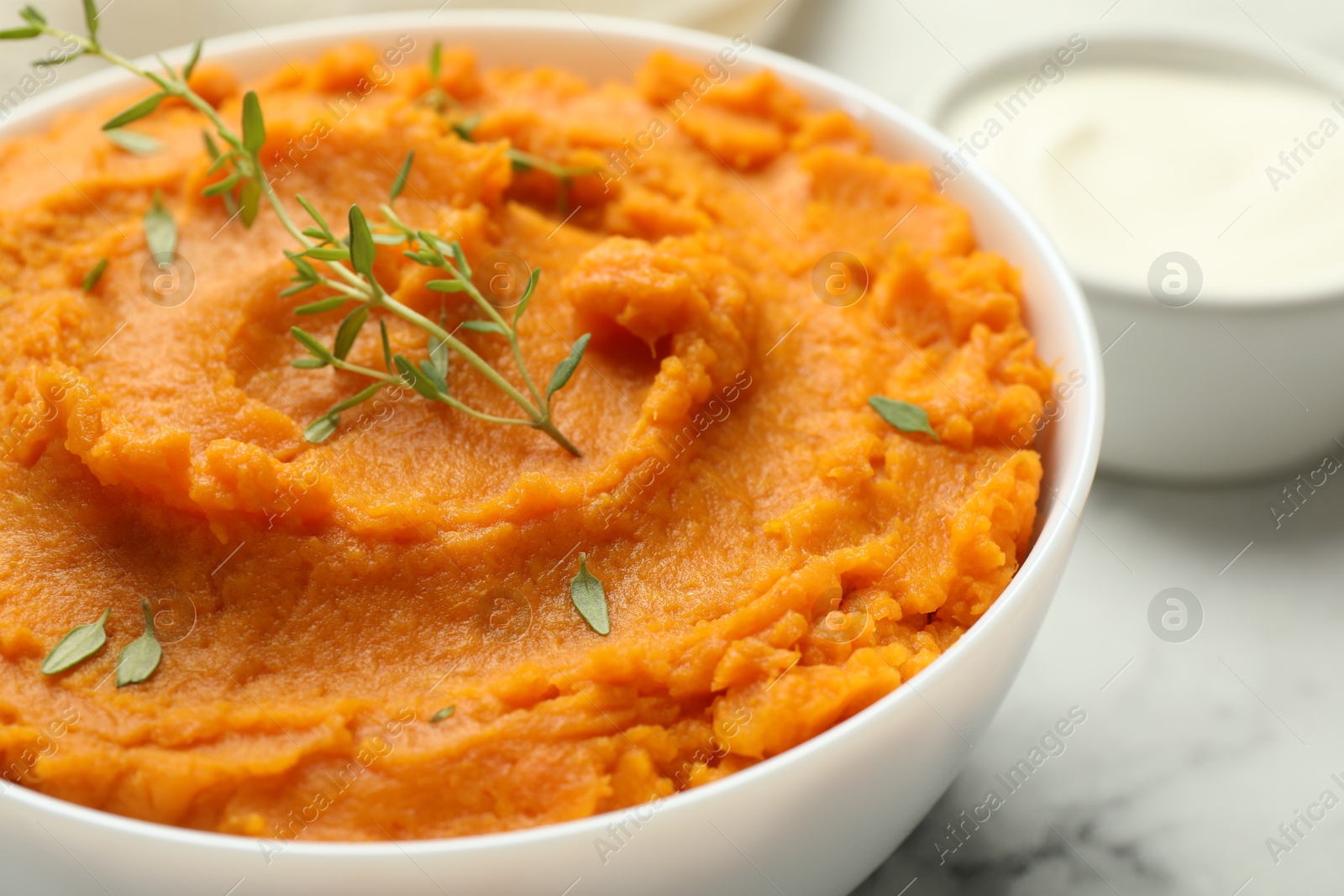 Photo of Delicious mashed sweet potatoes in bowl and microgreens on table, closeup