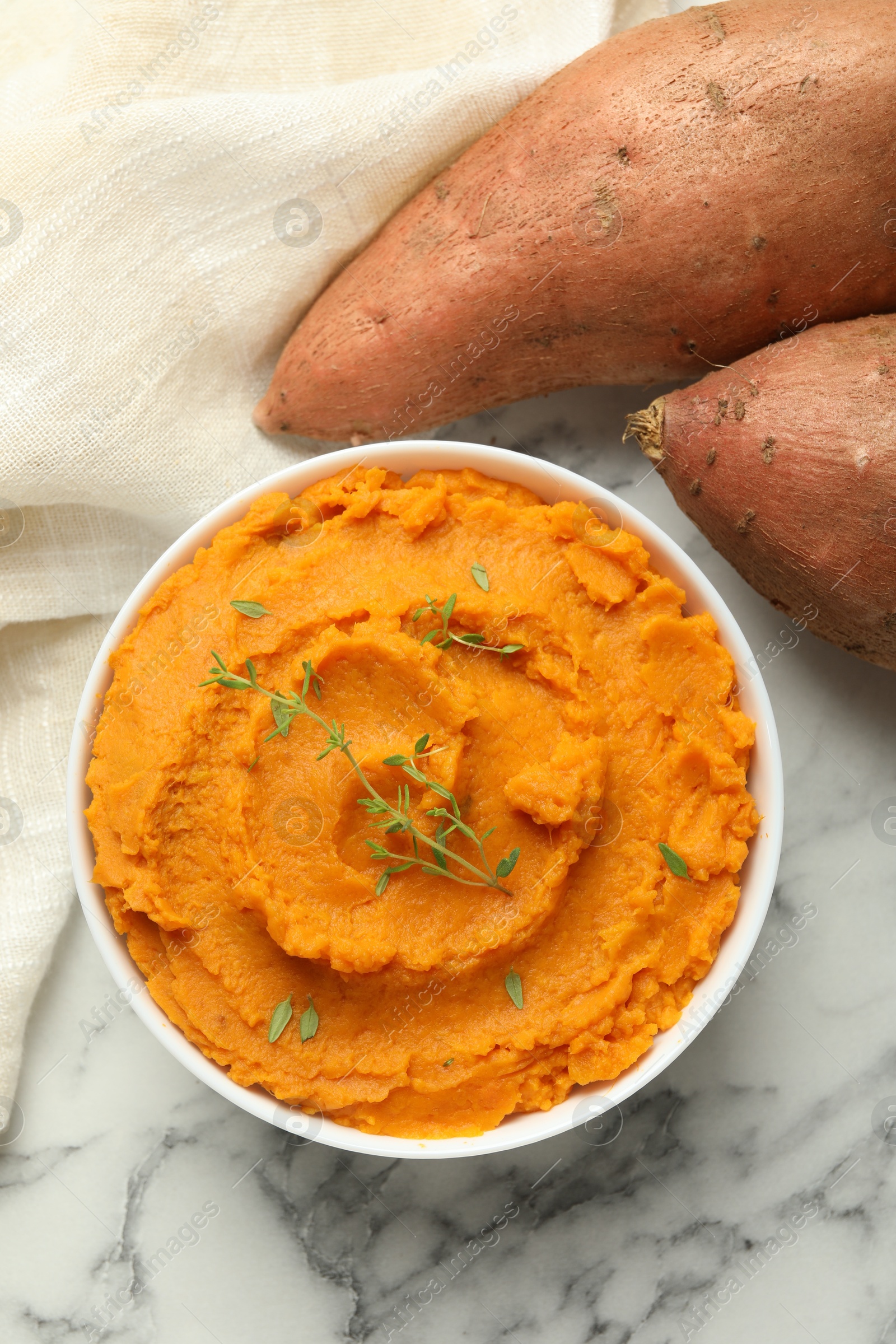 Photo of Delicious mashed sweet potatoes in bowl, microgreens and vegetables on white marble table, top view