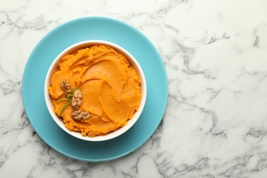 Photo of Delicious mashed sweet potatoes with walnuts in bowl on white marble table, top view. Space for text