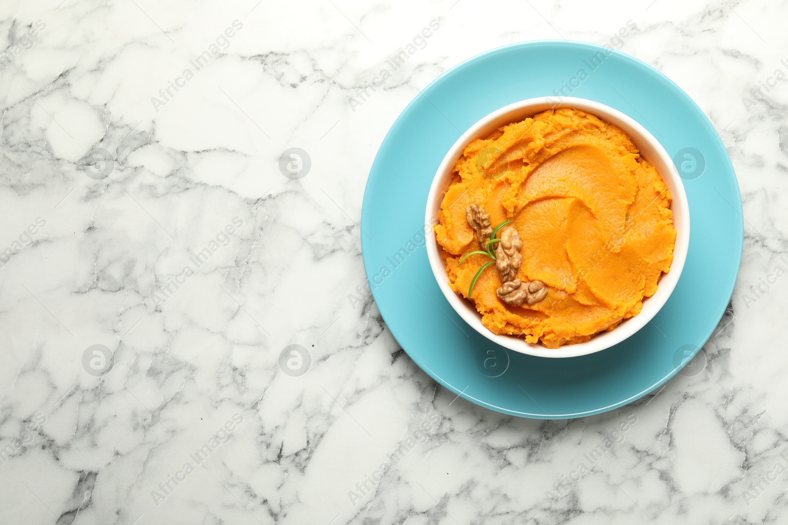 Photo of Delicious mashed sweet potatoes with walnuts in bowl on white marble table, top view. Space for text