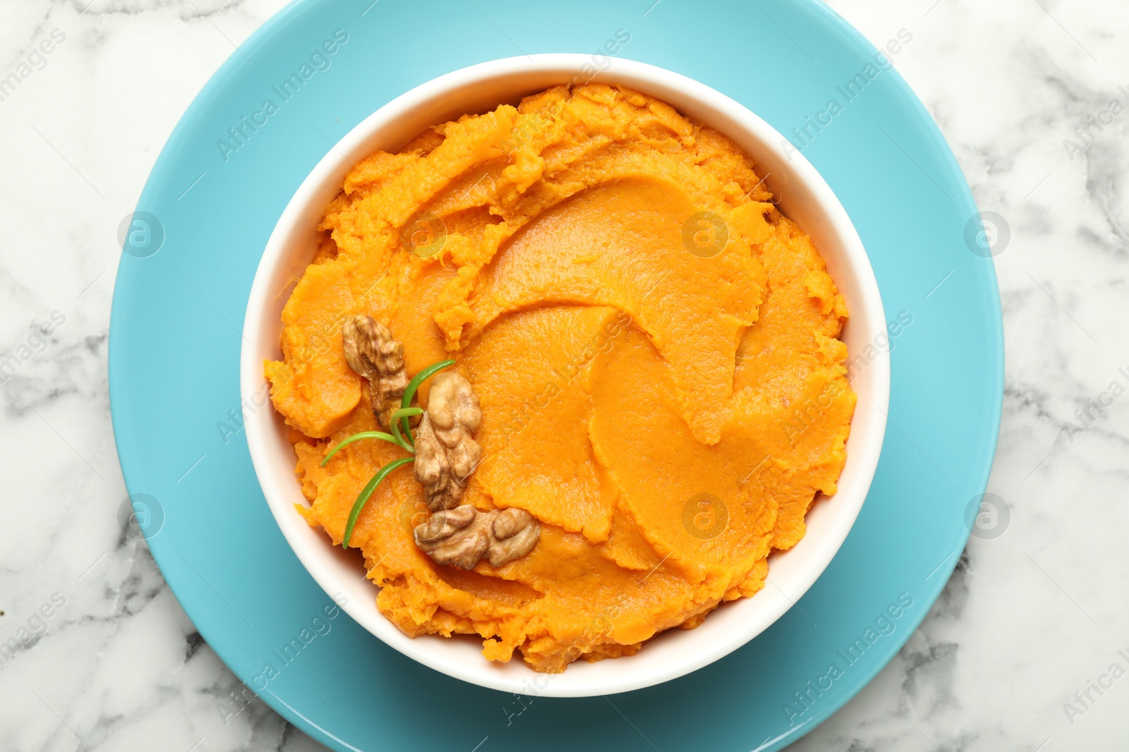 Photo of Delicious mashed sweet potatoes with walnuts in bowl on white marble table, top view