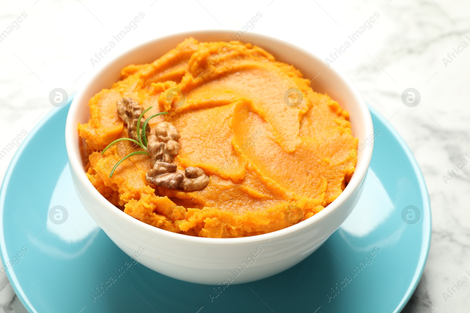 Photo of Delicious mashed sweet potatoes with walnuts in bowl on white marble table, closeup