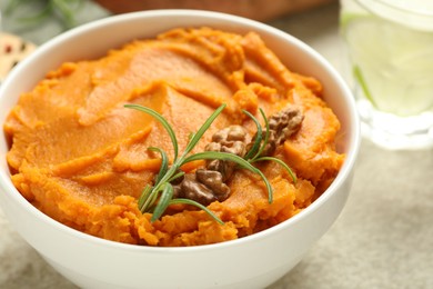 Photo of Delicious mashed sweet potatoes with walnuts and rosemary in bowl on light table, closeup