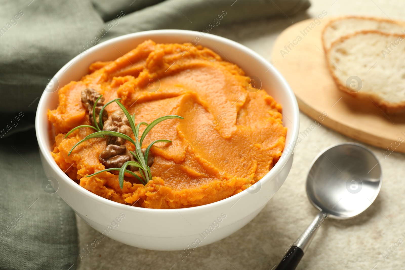 Photo of Delicious mashed sweet potatoes with walnuts, rosemary, spoon and bread on light table, closeup