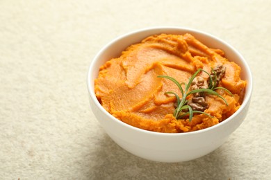 Photo of Delicious mashed sweet potatoes with walnuts and rosemary in bowl on light table, closeup. Space for text