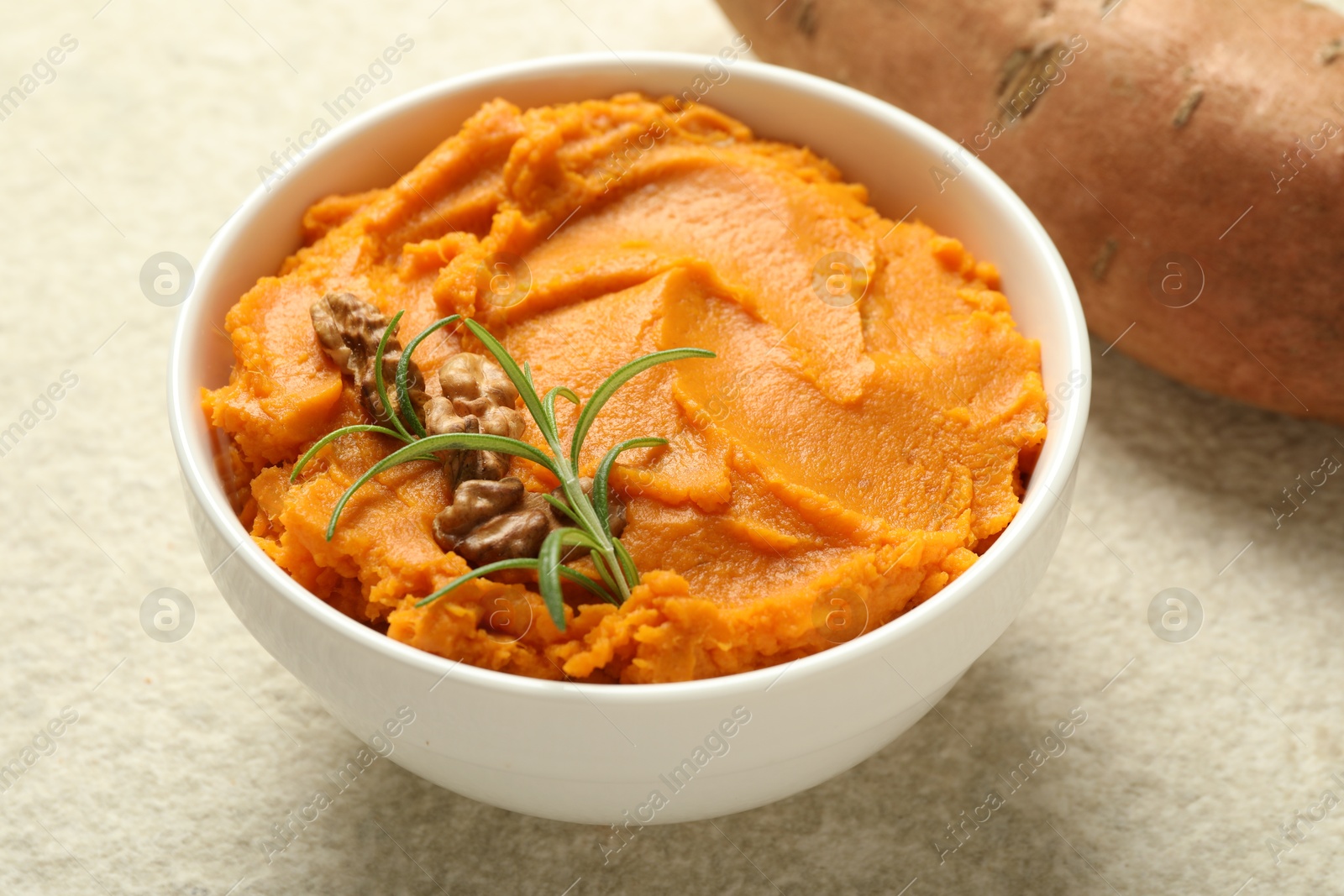 Photo of Delicious mashed sweet potatoes with walnuts and rosemary in bowl on light table, closeup