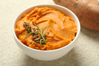 Delicious mashed sweet potatoes with walnuts and rosemary in bowl on light table, closeup