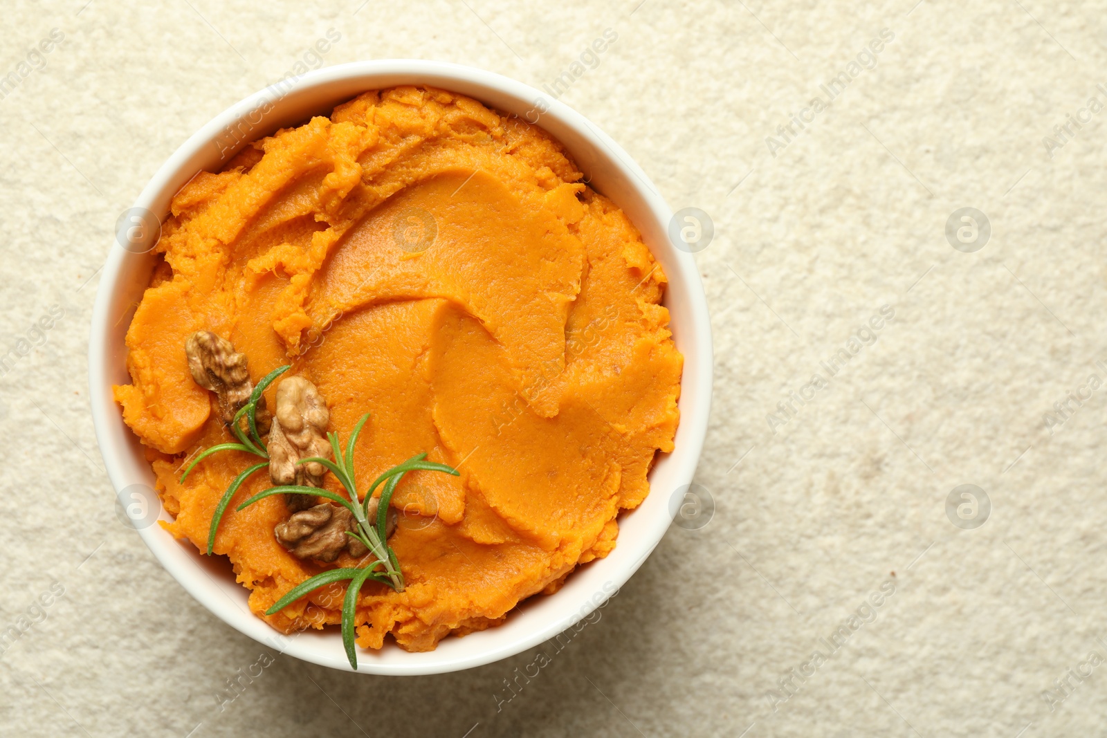 Photo of Delicious mashed sweet potatoes with walnuts and rosemary in bowl on light table, top view. Space for text