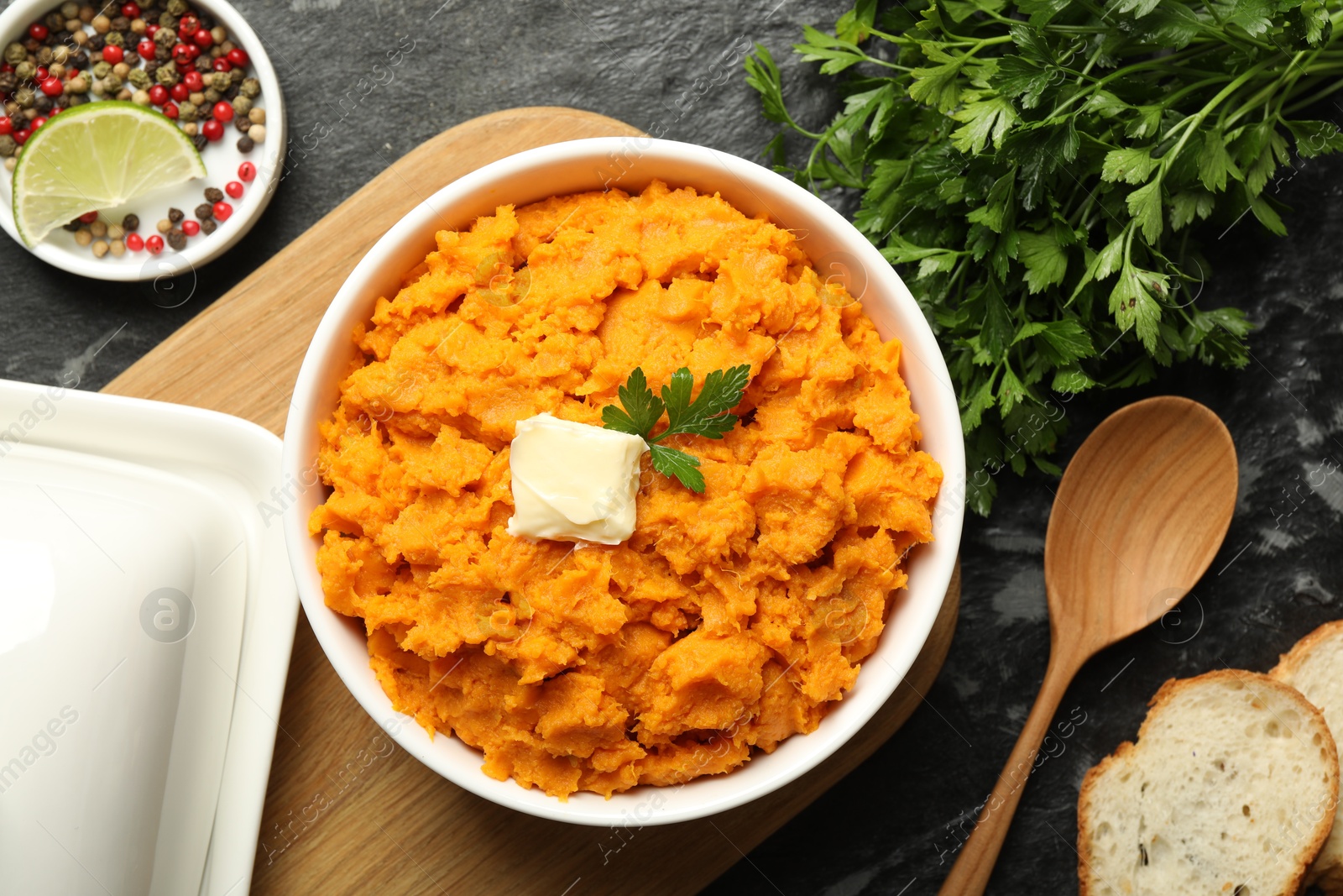 Photo of Delicious mashed sweet potatoes with butter, spices, bread and spoon on dark table, top view